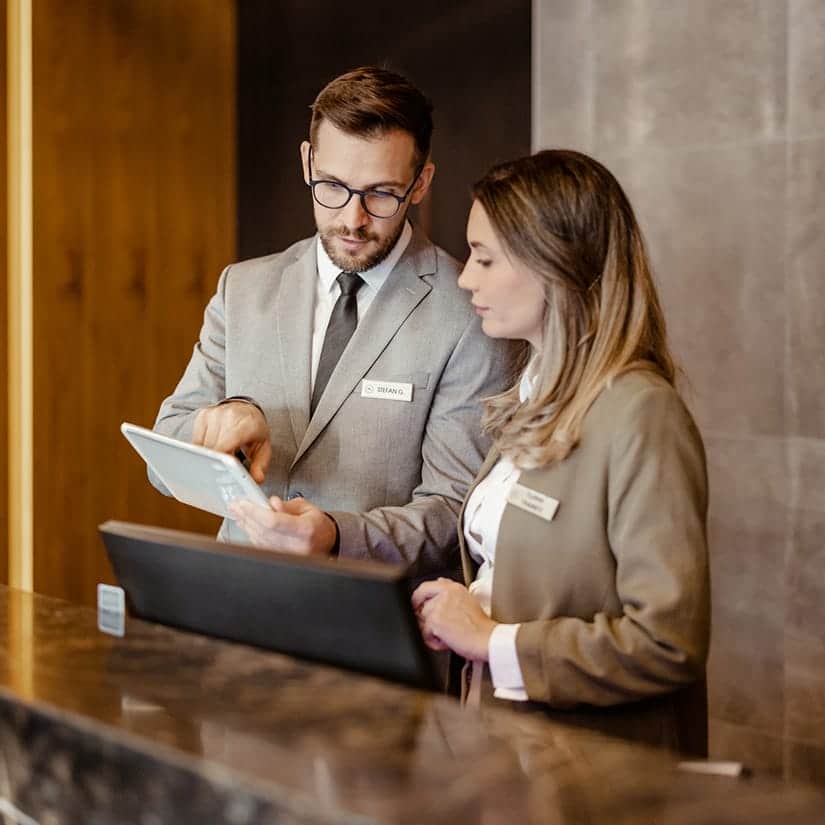 A man and woman standing at a desk looking at a tablet