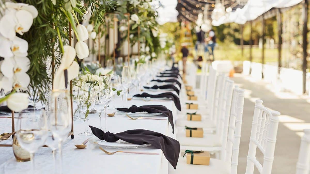 A long table with white chairs and black napkins