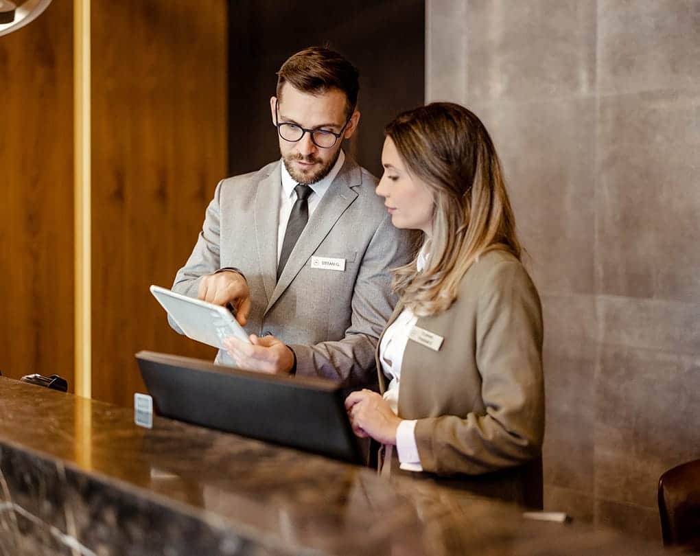 A man and woman standing at a desk looking at a tablet