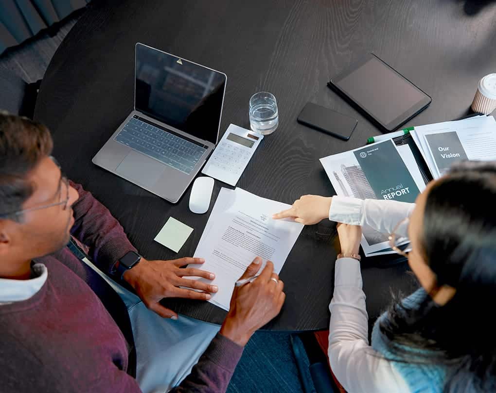 A man and woman sitting at a table with papers and laptops