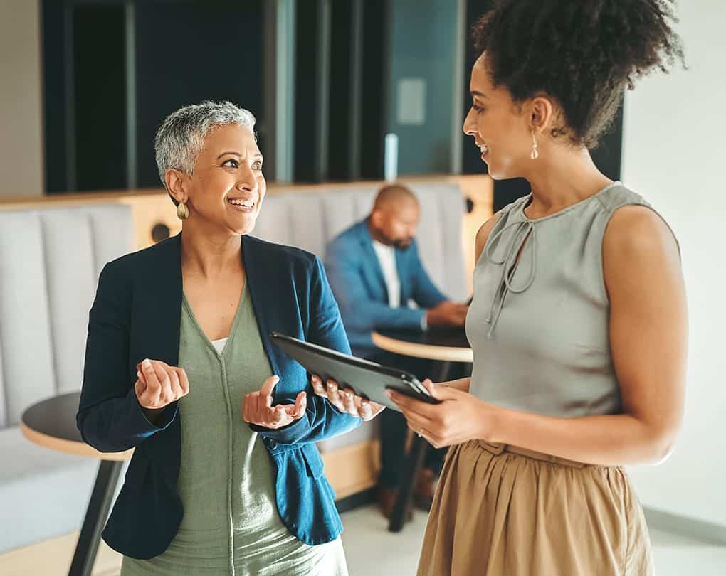A woman holding a tablet and talking to another woman