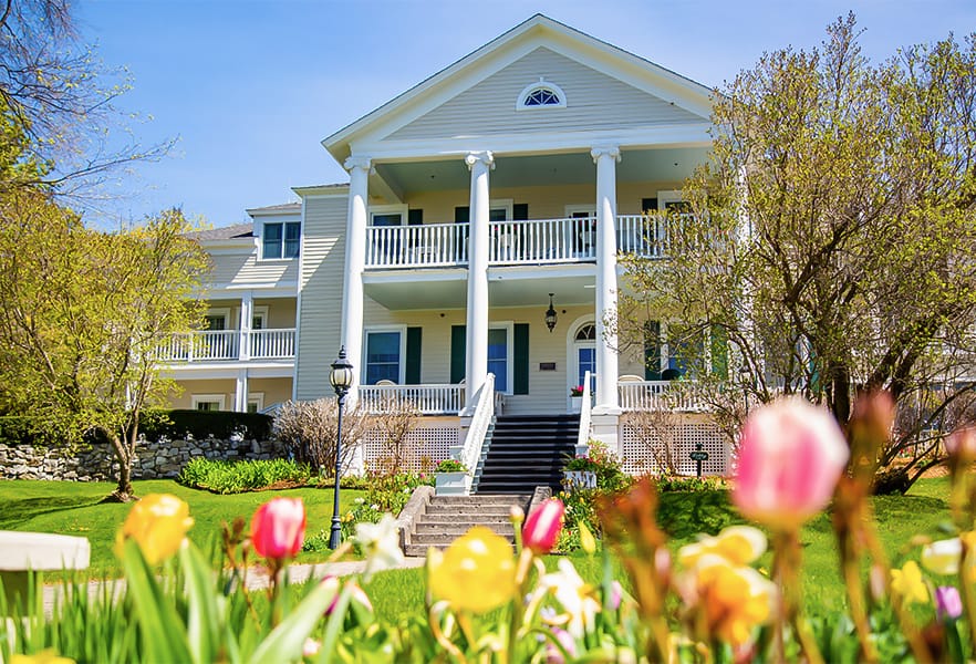 A house with a lawn and flowers with Seguine Mansion in the background