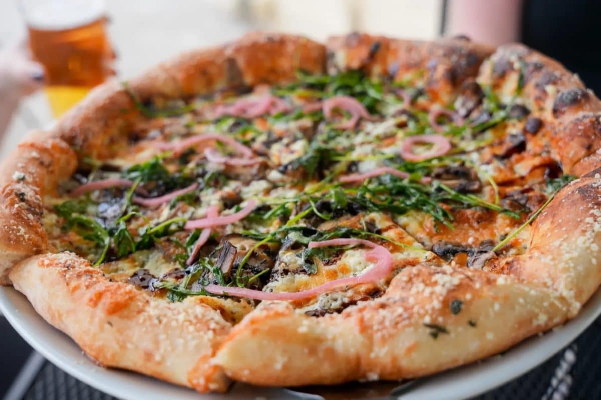 A wood-fired pizza topped with arugula and pickled onions